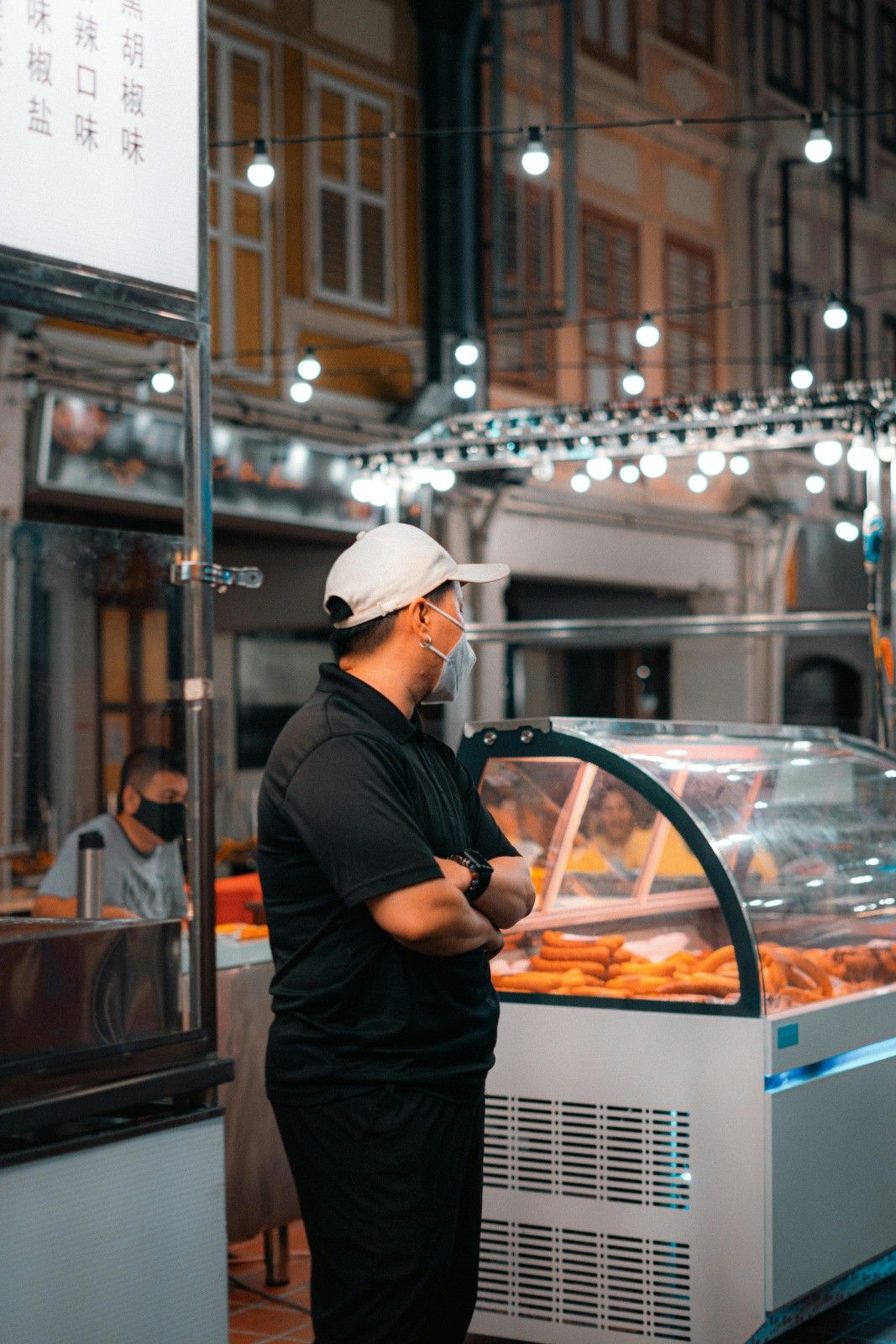 Vendor at a Singapore hawker center night market standing next to a food display case.