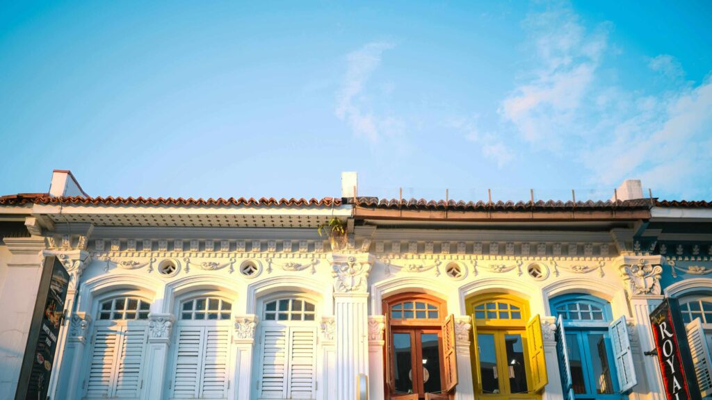 This image captures the colorful and ornate facades of traditional shophouses, likely in a Southeast Asian city like Singapore or Malaysia, under a bright blue sky.