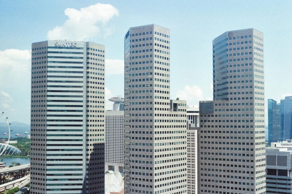 This image captures the distinctive high-rise office towers of Suntec City in Singapore, characterized by their geometric, faceted architecture and repetitive window patterns. In the background, other iconic landmarks like the Marina Bay Sands and the Singapore Flyer are visible under a bright, clear sky.