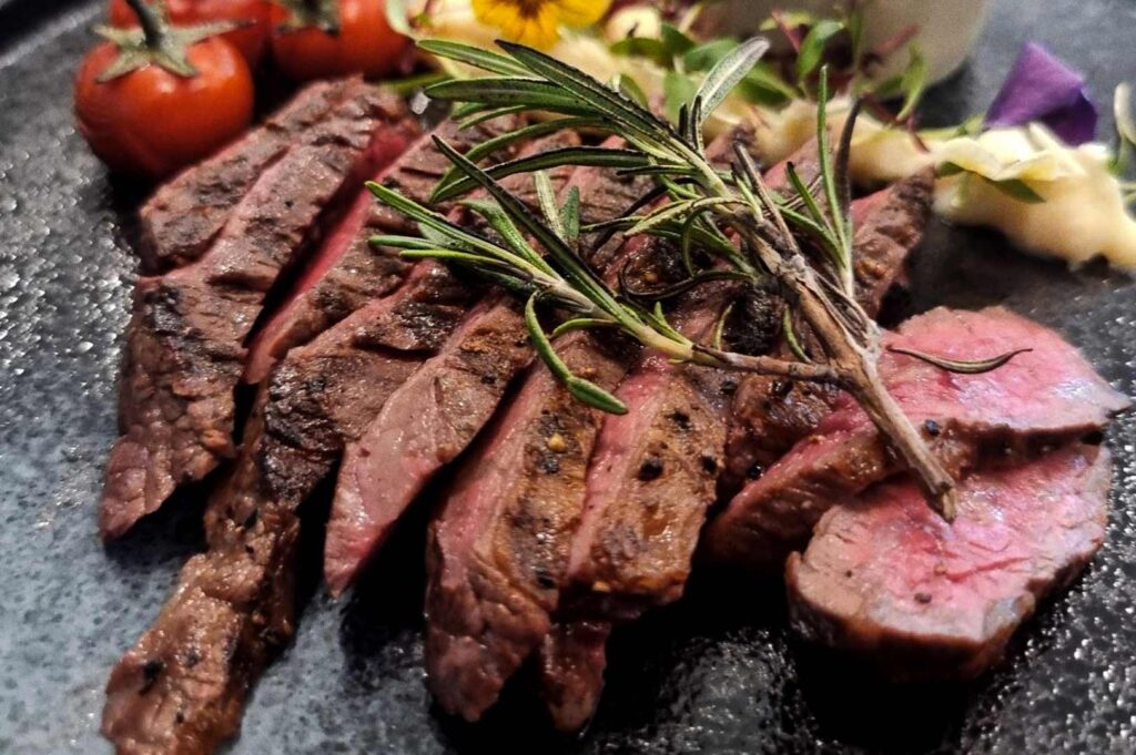 Gourmet grilled steak plated with rosemary garnish, roasted cherry tomatoes, creamy mashed potatoes, microgreens, and edible flowers.