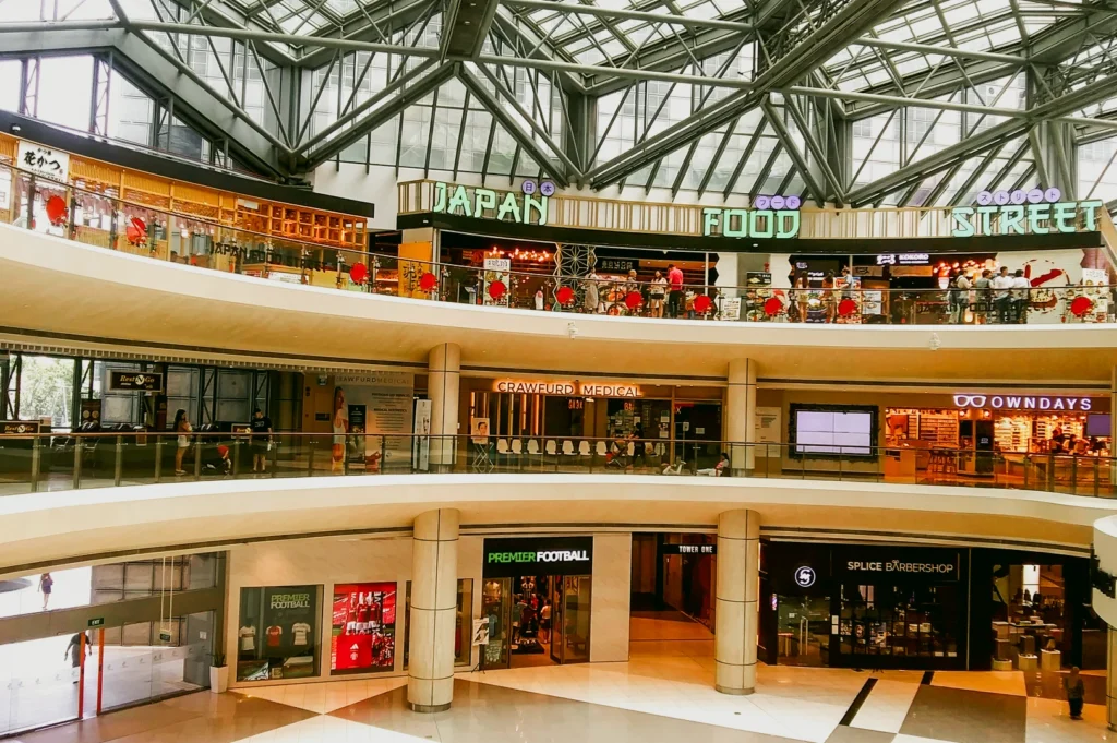 Wide-angle elevated shot of Suntec City Atrium in Singapore, featuring the Japan Food Street with illuminated restaurant signage, multi-level walkways, glass railings, and open atrium architecture.
