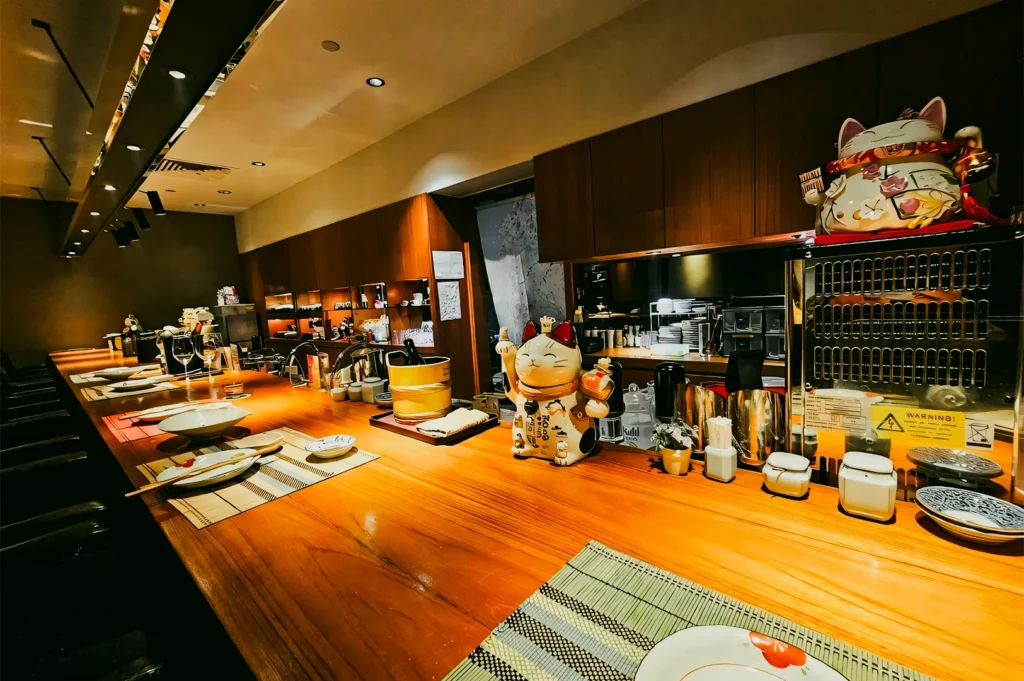 Wide-angle eye-level shot of Hanashizuku Japanese Cuisine sushi counter in Cuppage Plaza Singapore, featuring minimalist wood interior, warm lighting, and authentic Japanese dining setup
