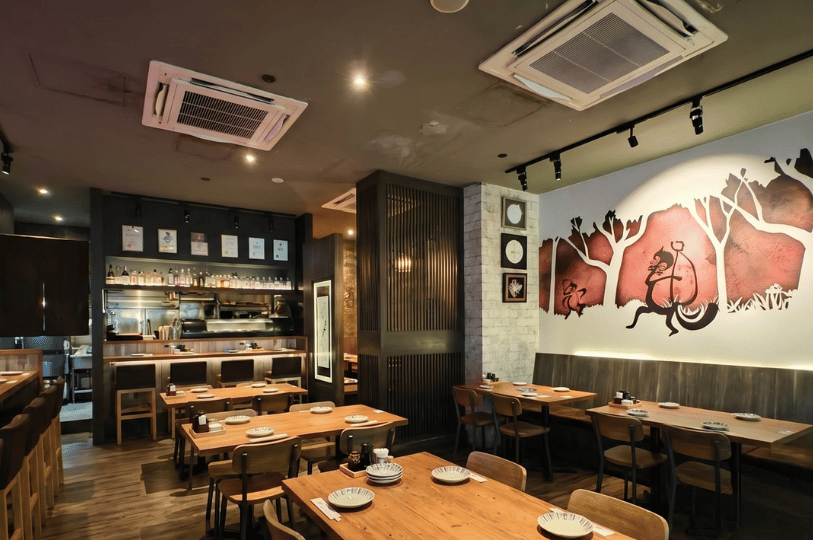 Warmly lit dining room at Shunjuu Izakaya featuring wooden tables and a large mural of a monkey on the wall.