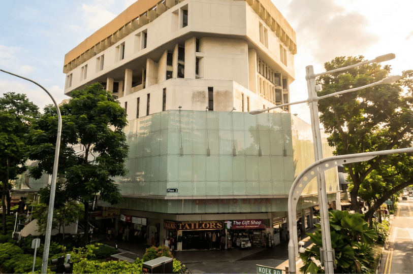 Exterior view of the Orchard Plaza building in Singapore during the day, highlighting its multi-story architectural facade and street-level shopfronts.