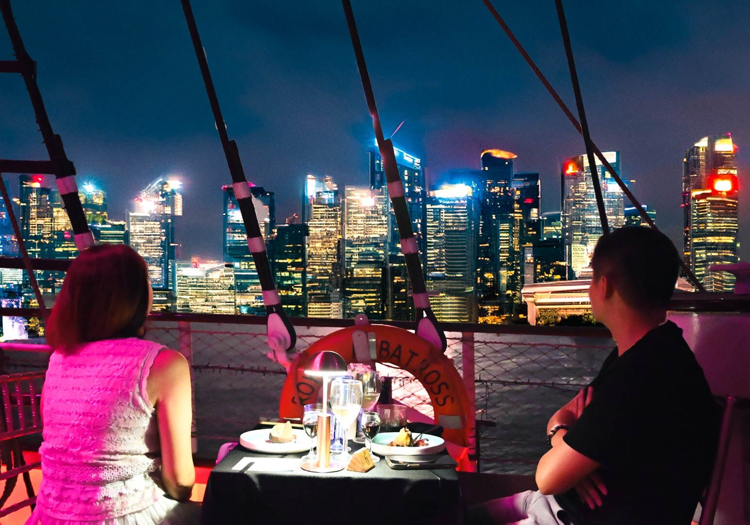 Romantic rooftop dining overlooking the Singapore skyline on a luxury ship deck.