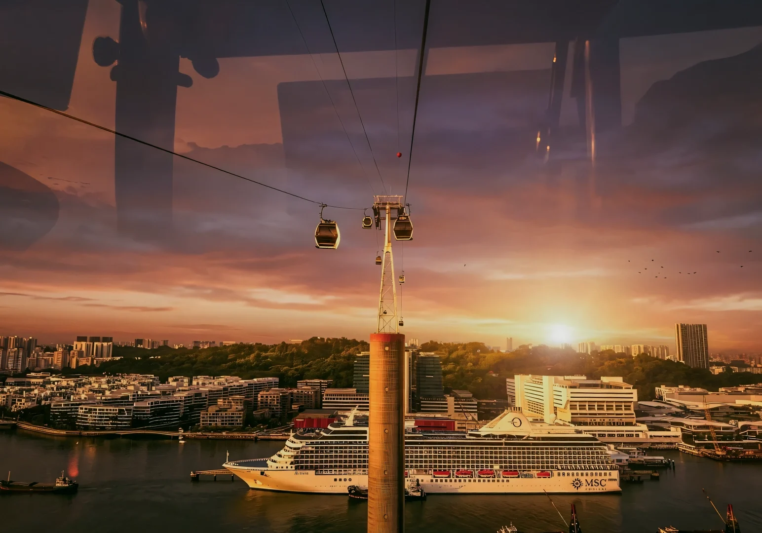 Wide-angle front-facing shot from inside Singapore cable car showing sunset skyline, Mount Faber Lodge aerial view, harbor cruise ship and cityscape – Cable Car Sky Dining experience Singapore.