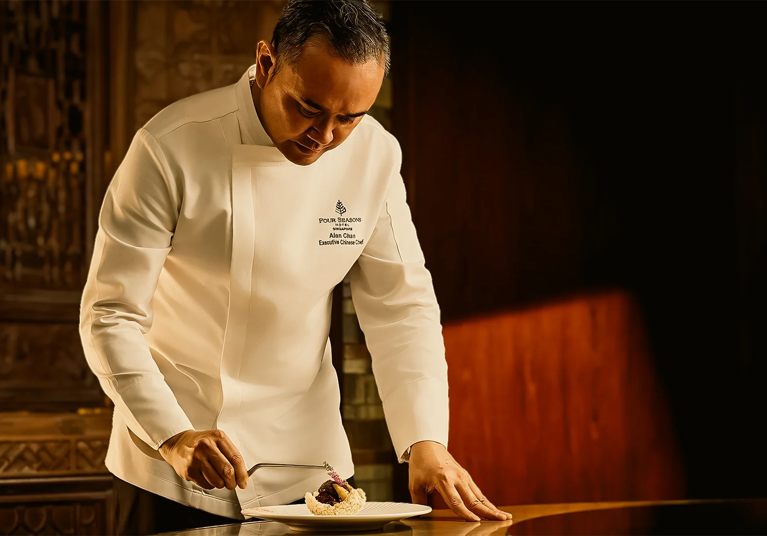 Medium close-up side-angle shot of professional chef plating gourmet dish at luxury Chinese restaurant in Singapore showcasing modern Cantonese cuisine