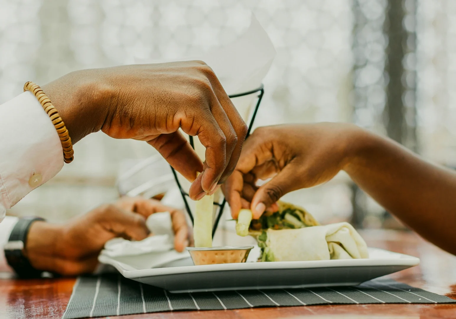 Eye-level close-up of two people sharing a meal at a restaurant, hands reaching toward a plate of food, capturing intimacy, connection, and dining as a love language.