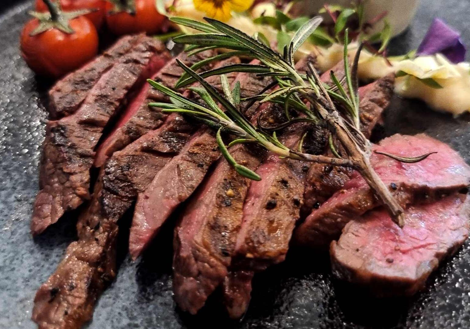Gourmet grilled steak plated with rosemary garnish, roasted cherry tomatoes, creamy mashed potatoes, microgreens, and edible flowers.