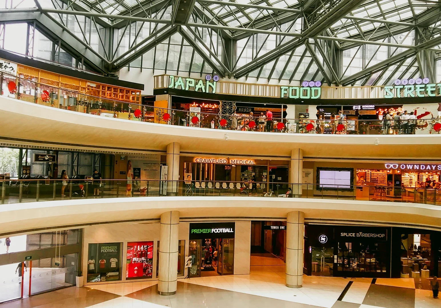 Wide-angle elevated shot of Suntec City Atrium in Singapore, featuring the Japan Food Street with illuminated restaurant signage, multi-level walkways, glass railings, and open atrium architecture.