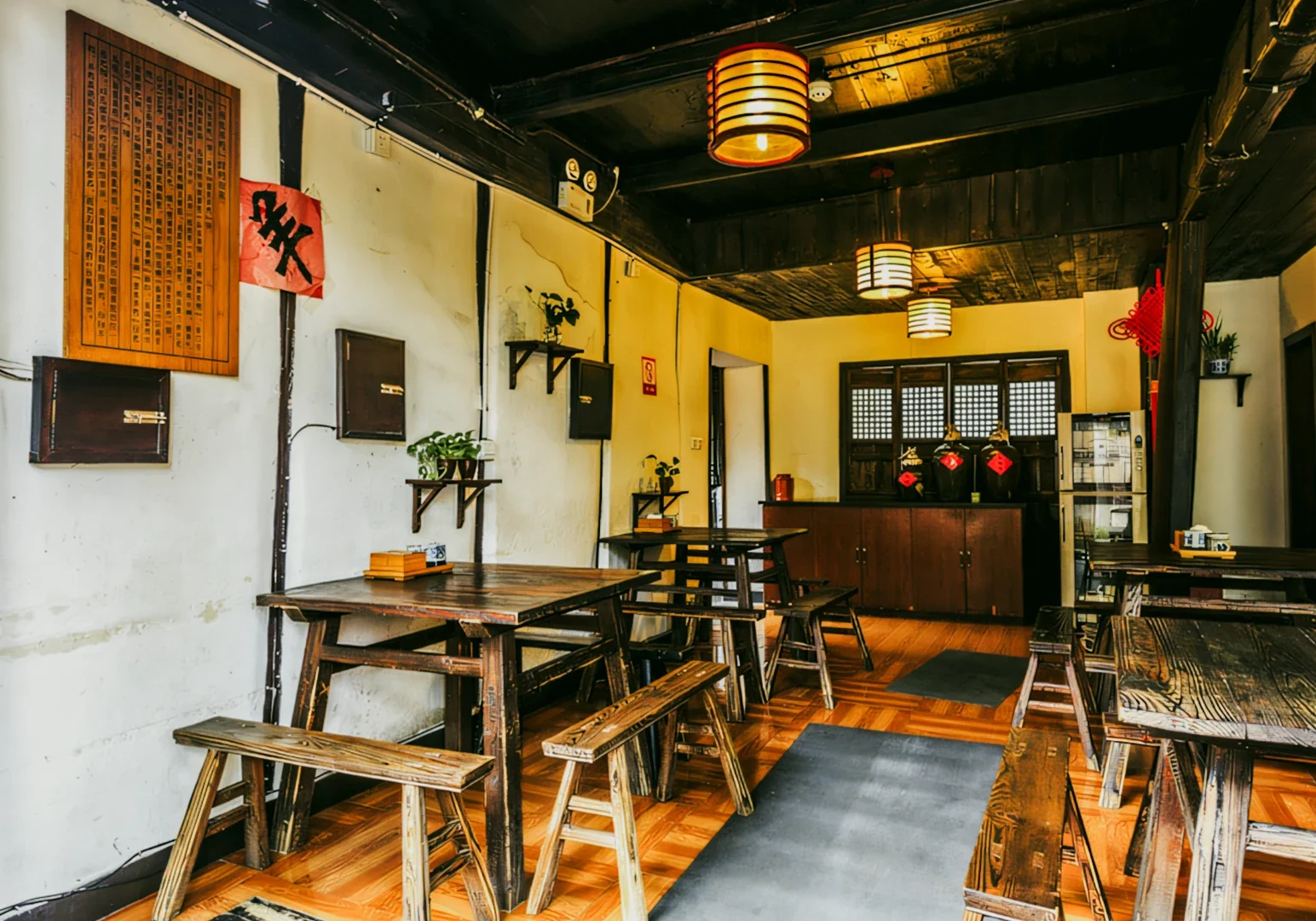 Wide-angle interior shot of a traditional-style restaurant dining space with rustic wooden tables and benches, warm hanging lantern lights, wooden flooring, and decorative wall accents, showcasing cultural ambiance and authentic restaurant design.