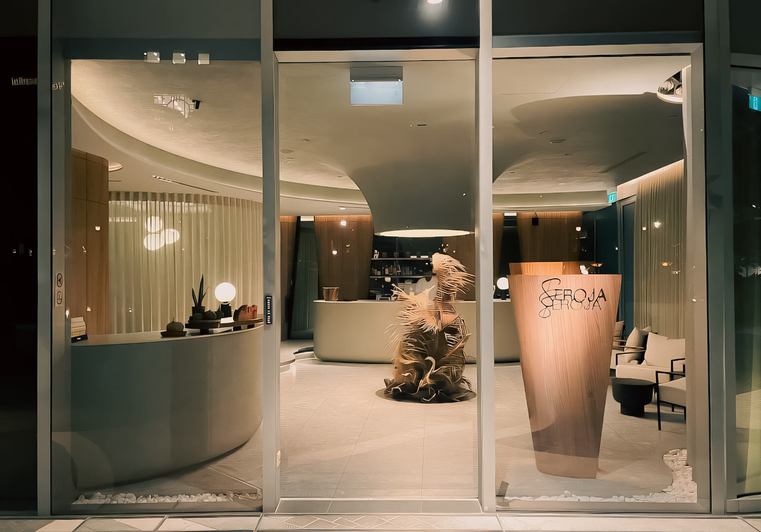 Elegant restaurant entrance with floor‑to‑ceiling glass windows, modern curved interior design elements, and the Seroja signage displayed on a wooden panel.