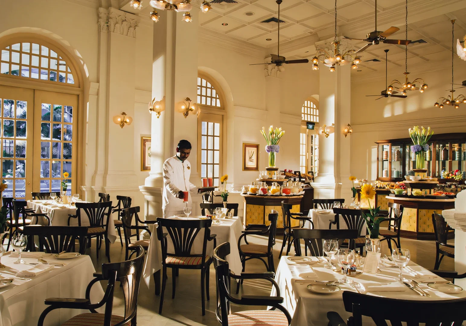 1 Singapore’s Culinary Past Restaurants Wide‑angle interior shot of an elegant heritage restaurant with high ceilings, arched windows, white tablecloth dining tables, classic wooden chairs, and warm ambient lighting, showcasing Singapore’s colonial‑era dining atmosphere and refined culinary history.