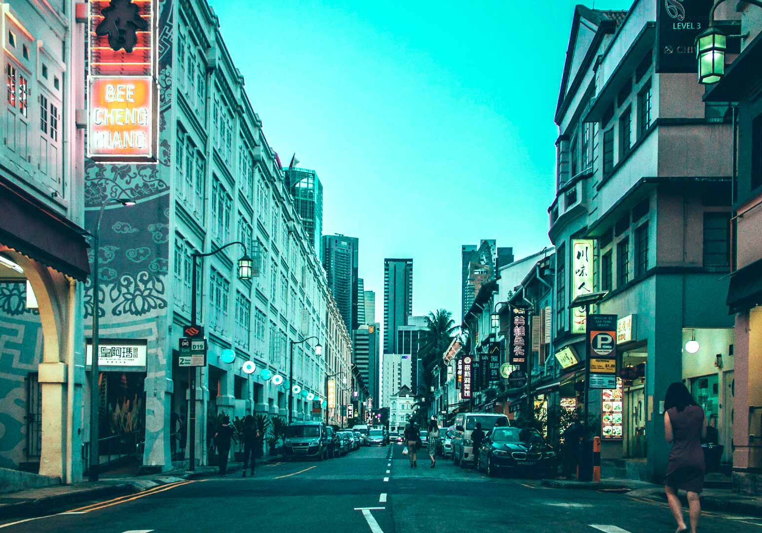 1-Tanjong-Pagar Nighttime city street on Tanjong Tagar featuring neon storefronts, cultural signage, pedestrians, and a contrast of low-rise shops and tall towers.
