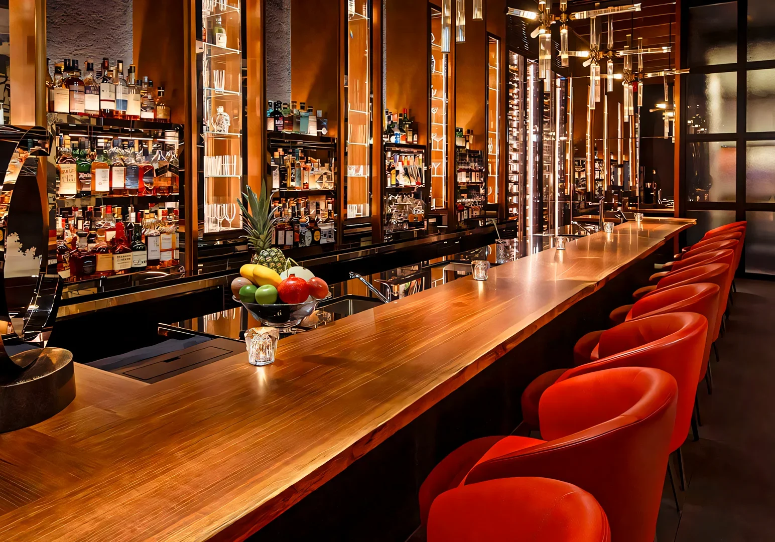 High‑end cocktail bar with a long polished wooden counter, red upholstered bar stools, and backlit shelves filled with premium spirits.
