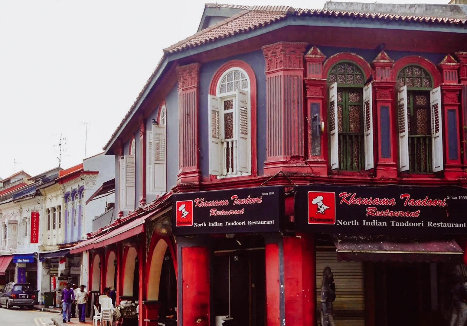 Eye‑level wide shot of a heritage shophouse restaurant in Little India, Singapore, featuring colorful colonial architecture and the exterior of a well‑known North Indian tandoori restaurant along a historic street.