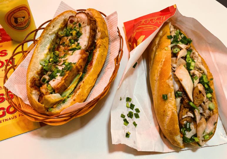 11-orchard-plaza-stalls Two hearty Vietnamese banh mi sandwiches, one featuring thick slices of crispy roasted pork in a basket and the other packed with assorted meats and herbs, served next to a Miss Saigon branded drink.