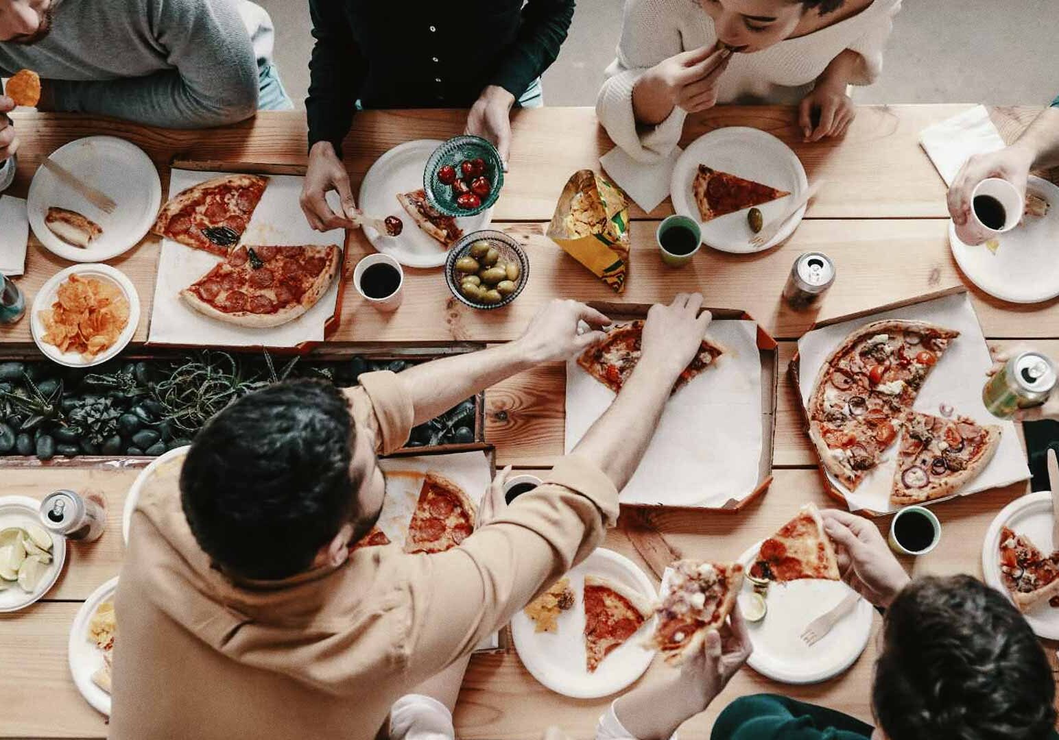 Group sharing pizza and snacks on a rustic wooden table.