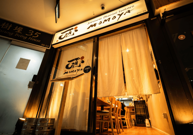 12-orchard-plaza-stalls The warm, inviting entrance of Momoya Japanese Obanzai Izakaya at Orchard Plaza, showcasing traditional white noren curtains over glass sliding doors and a wooden signboard.