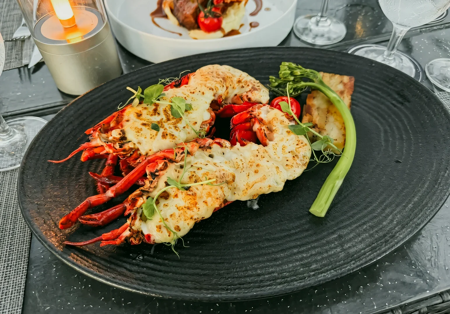 Close-up top-down angle of lobster thermidor plated on black dish during Cable Car Sky Dining at Mount Faber Lodge Singapore fine dining experience.