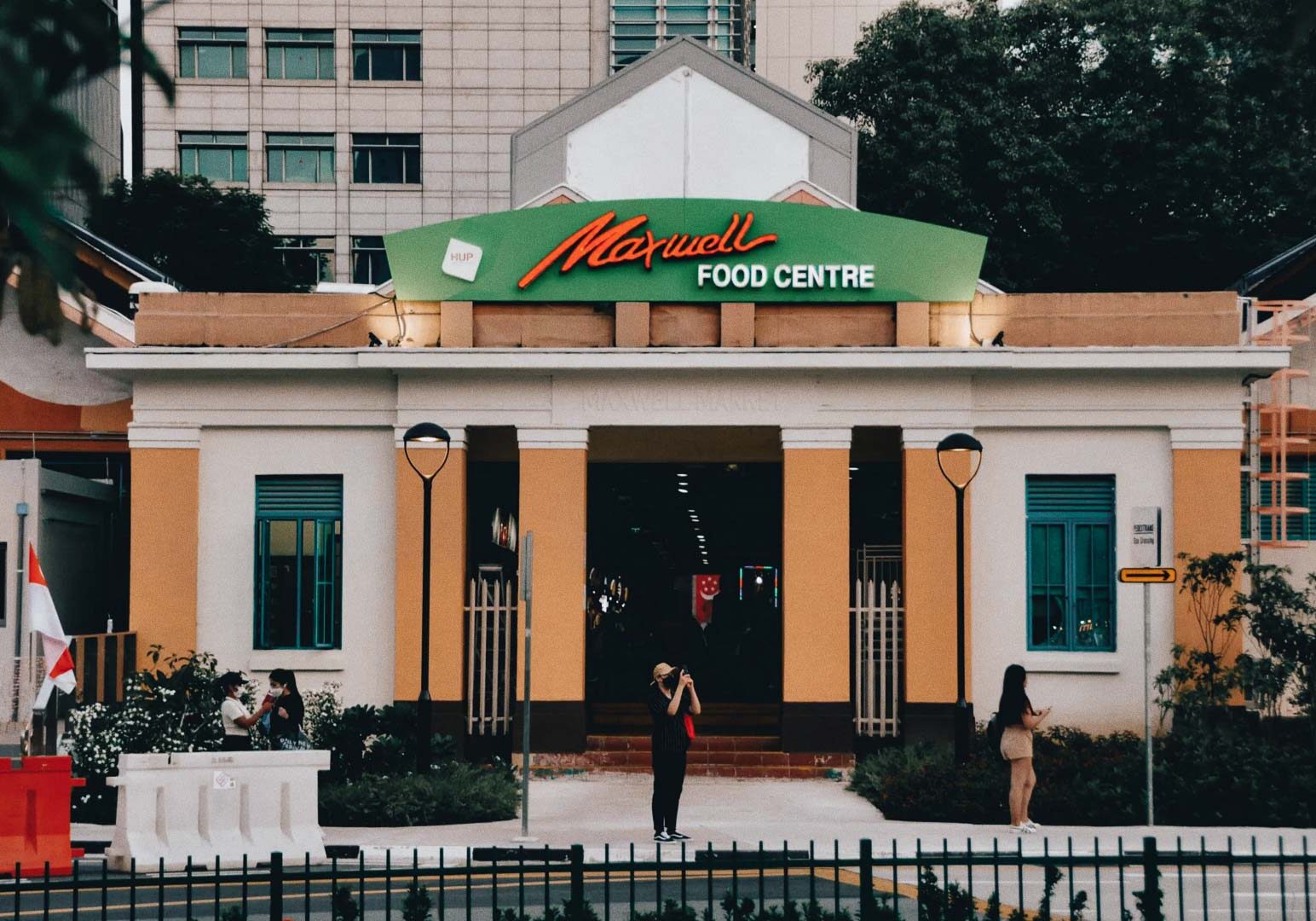 Front view of Maxwell Food Centre showing its iconic green signboard, colonial‑style architecture, and visitors entering the hawker centre.