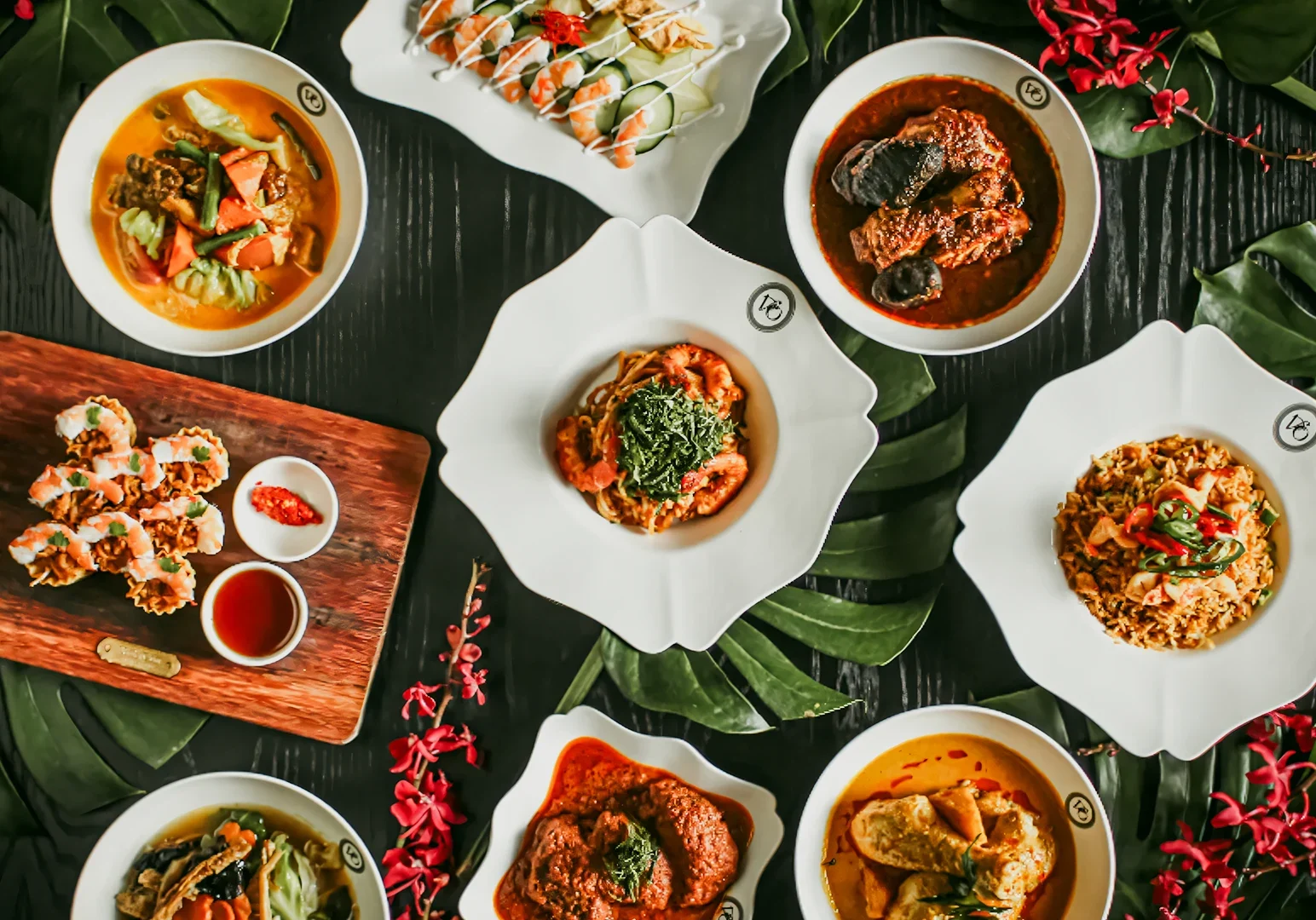 Overhead flat-lay shot of a Peranakan food spread featuring assorted Nyonya dishes with rich curries, sambal, and vegetables served on white plates.