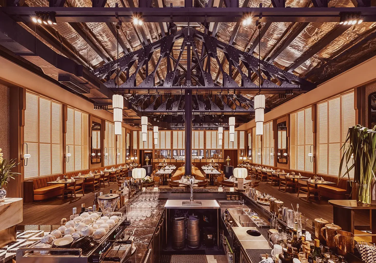 2 Jiak Kim House Singapore Elegant interior of Jiak Kim House featuring a high vaulted ceiling, exposed beams, a central bar counter, warm ambient lighting, and neatly arranged dining tables.