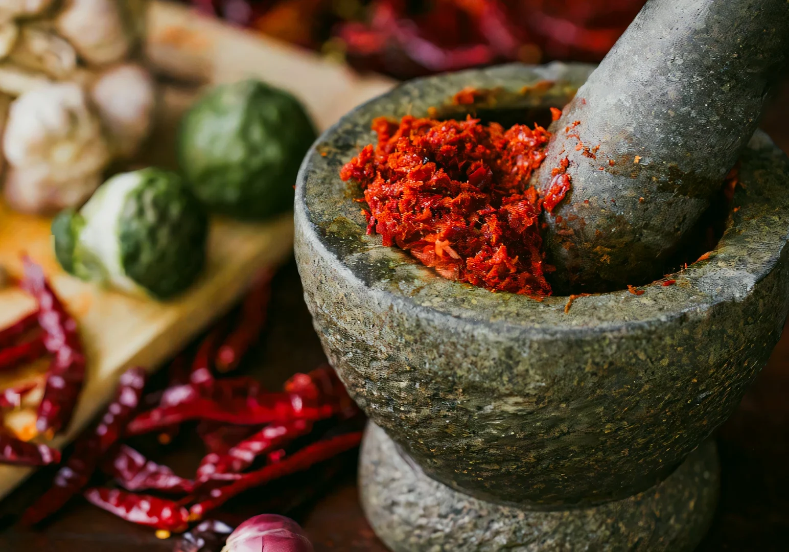 2 The Dedication Behind Peranakan Cuisine Singapore Through a Chef’s Work Macro close-up shot of rempah spice paste being ground with a stone mortar and pestle, surrounded by dried chilies, garlic, and herbs used in traditional Peranakan cooking.