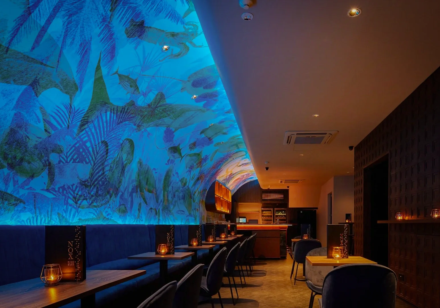 Wide-angle interior shot of an upscale lounge restaurant with curved ceiling mural, ambient lighting, booth seating, and intimate dining atmosphere.