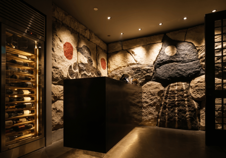 Sleek interior reception area at Tomo Tokyo, showcasing a minimalist black host stand against a rustic stone-textured accent wall with bold, stylized black and red artwork.