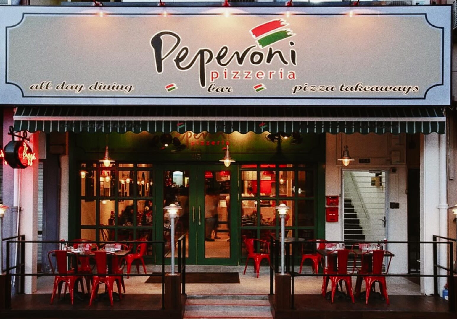 Peperoni Pizzeria storefront with outdoor seating and vibrant red chairs.
