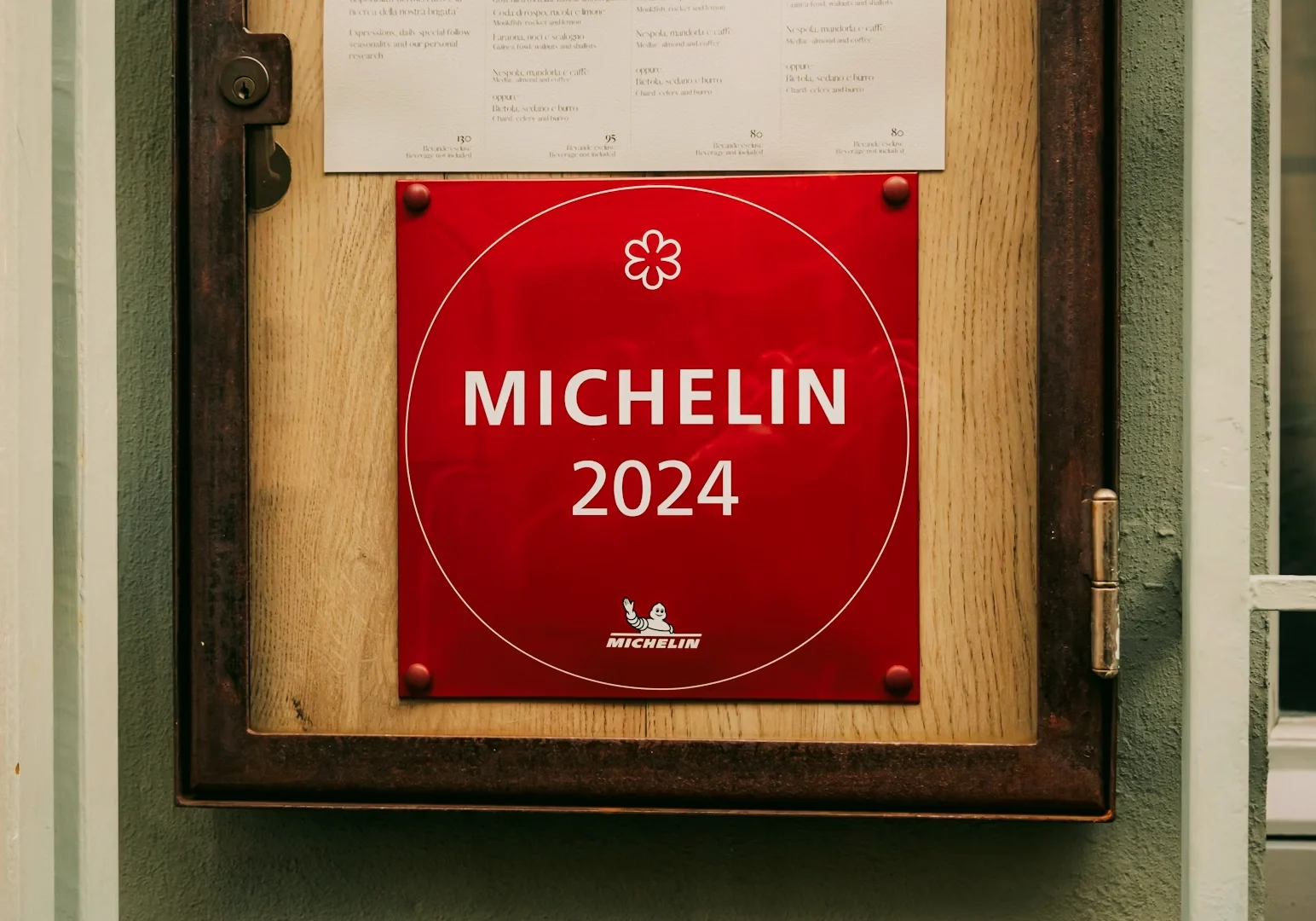 Eye-level frontal shot of a red Michelin Guide 2024 plaque displayed outside a restaurant, indicating Michelin recognition and culinary excellence.