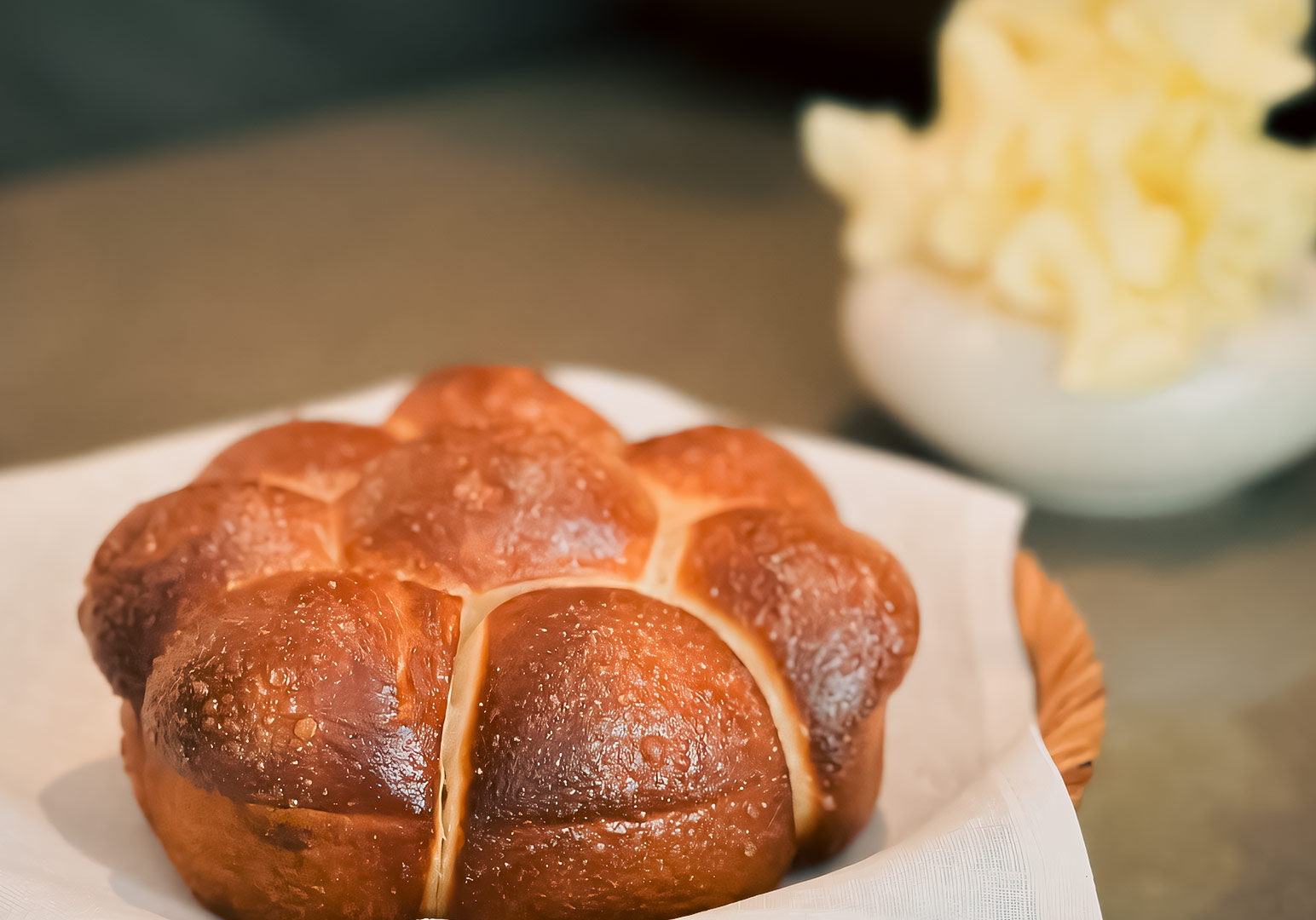 Golden brown pull‑apart bread, Roti Paung served on white cloth with a blurred bowl of johorean milk butter in the background.