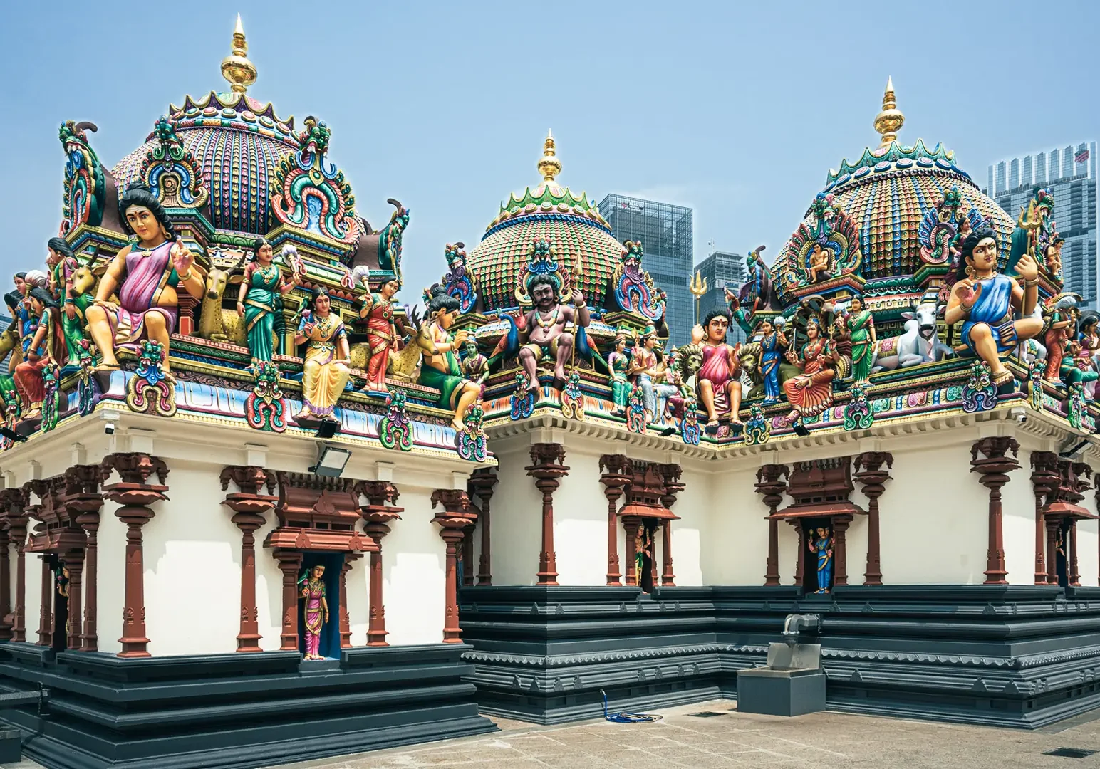 Colorful exterior of the Sri Mariamman Temple in Singapore, featuring intricate Hindu sculptures and ornate temple domes against a clear sky.