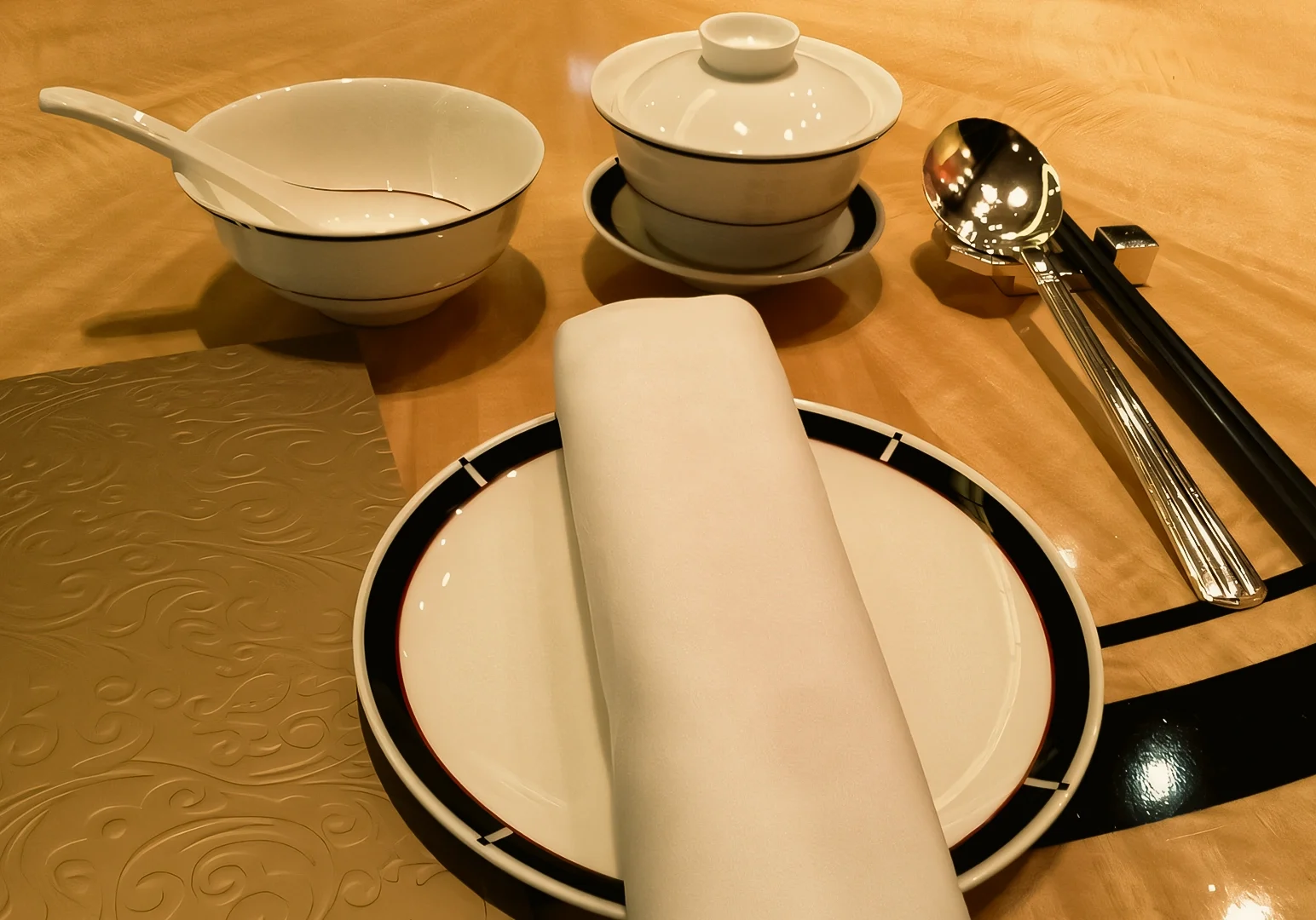 Close-up top-down shot of elegant Chinese restaurant table setting with porcelain bowl, teacup, chopsticks, and spoon at fine dining Cantonese restaurant in Singapore