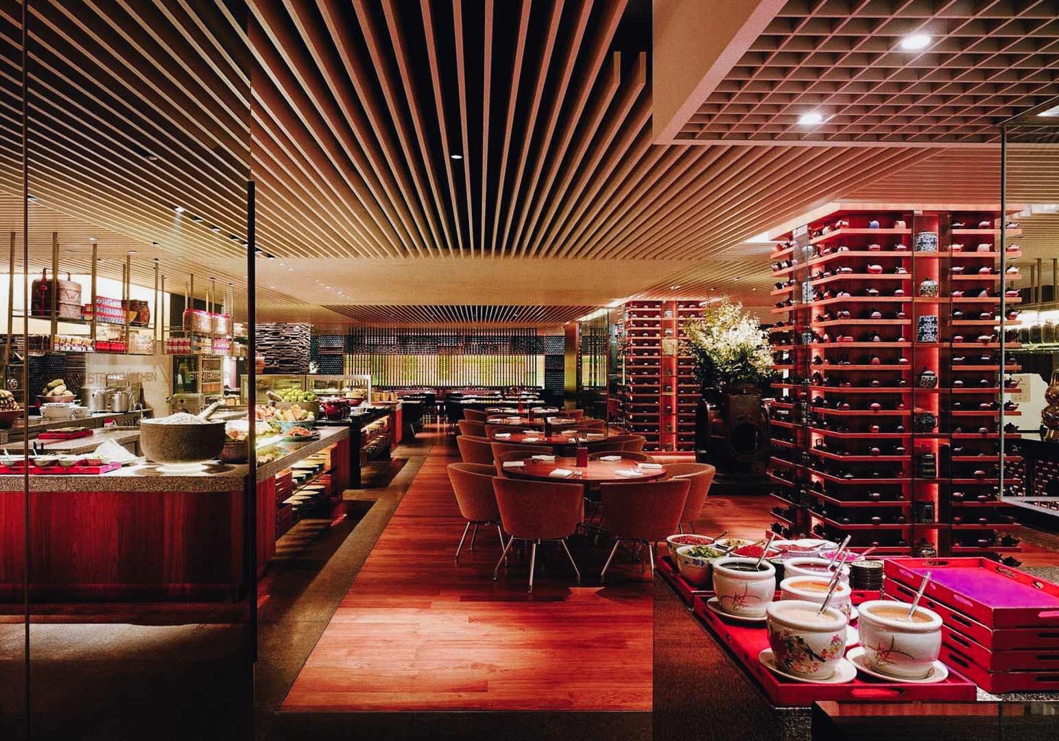 High‑end hotel buffet restaurant with warm lighting, decorative wooden panel ceilings, extensive food counters, and elegant dining tables.