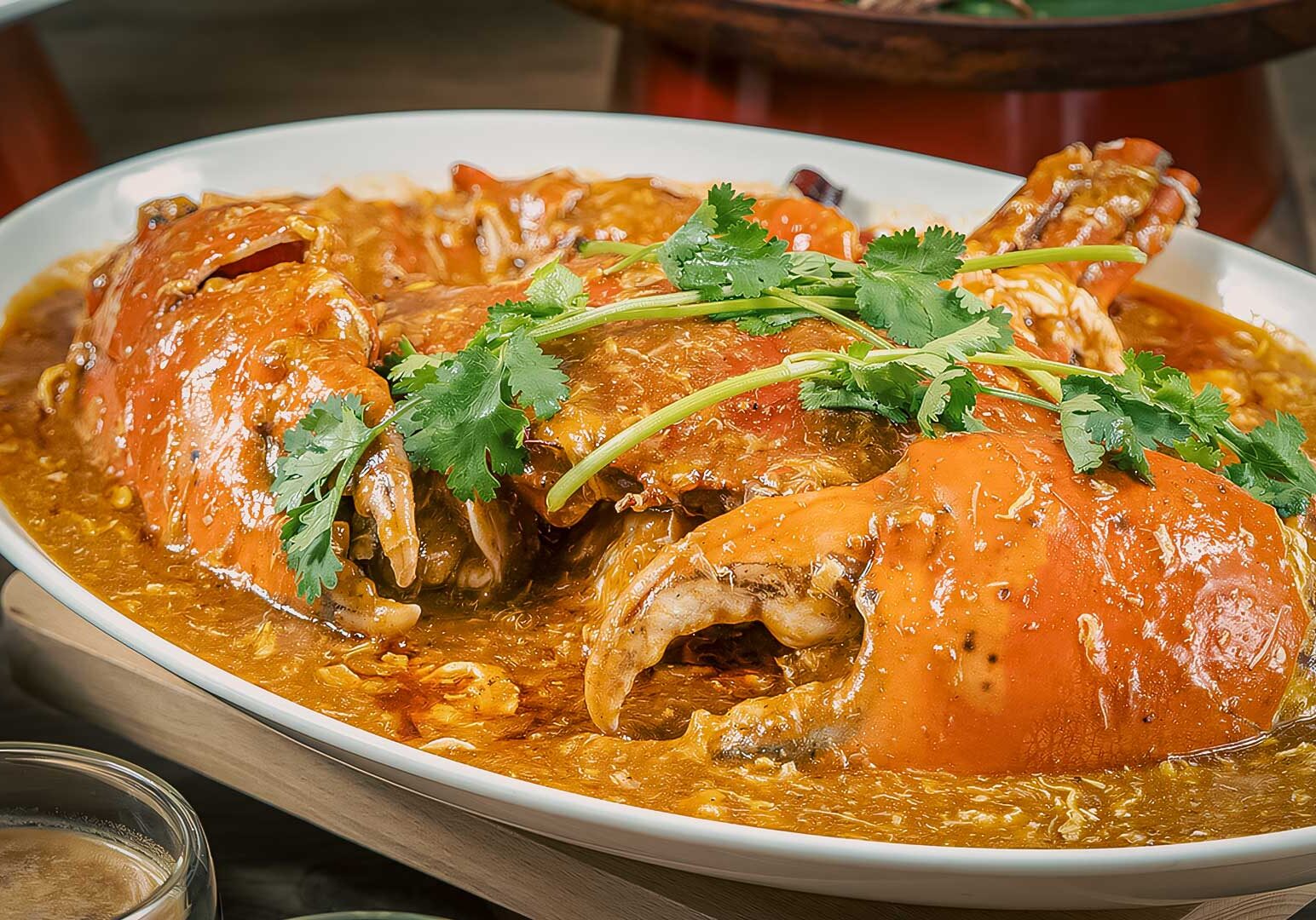 4-Palm-Beach-Seafood Singapore-style chili crab served on a large white platter, featuring whole crab cooked in a rich, spicy‑sweet chili gravy and garnished with fresh coriander