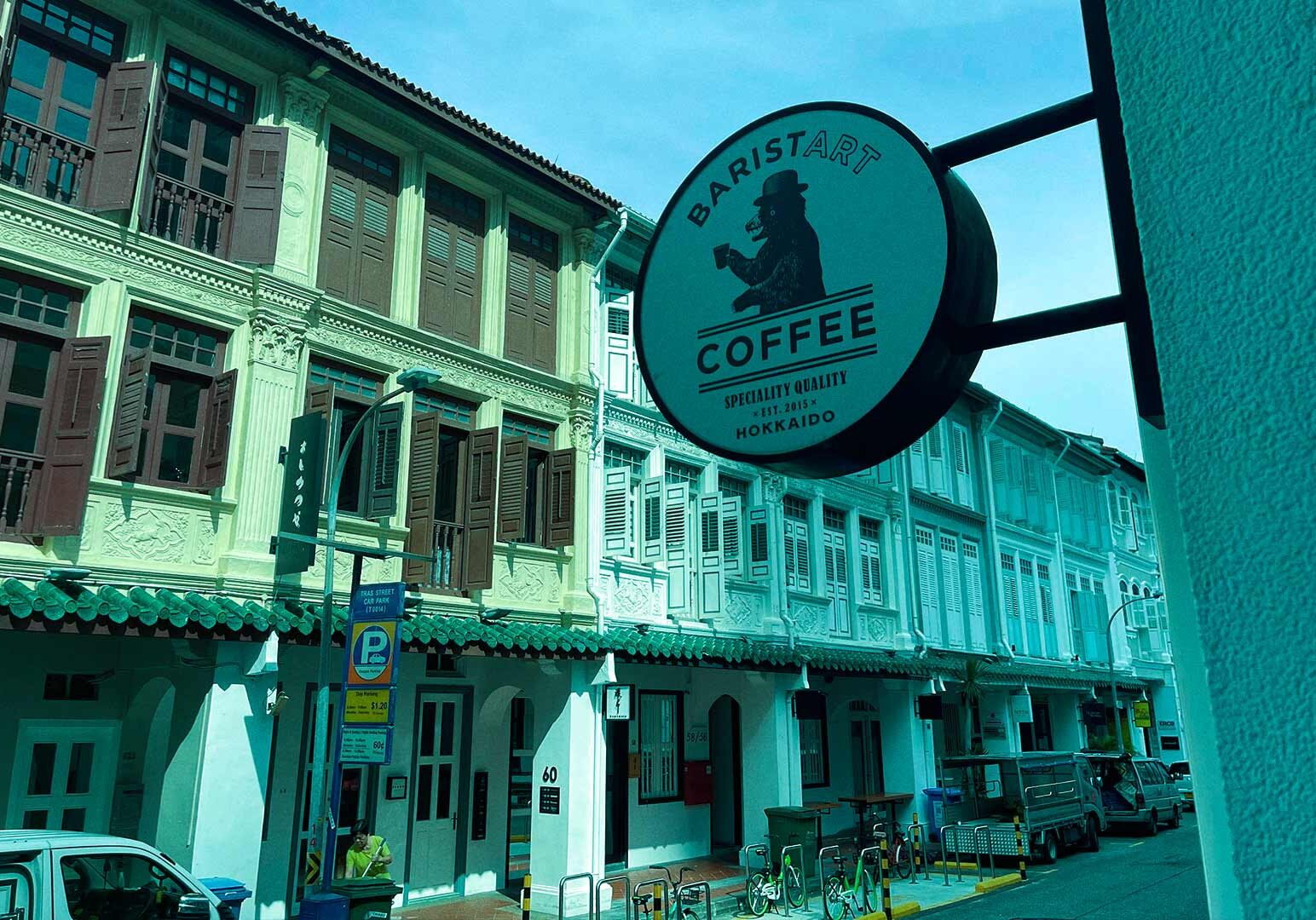 4-Tanjong-Pagar Street view of pastel shophouses with a prominent Baristart Coffee sign, parked cars, bicycles, and pedestrians in a historic urban district.