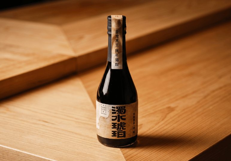 Close-up shot of a premium small dark glass bottle of artisanal Japanese sauce or sake with a traditional paper label, resting on a wooden tabletop.