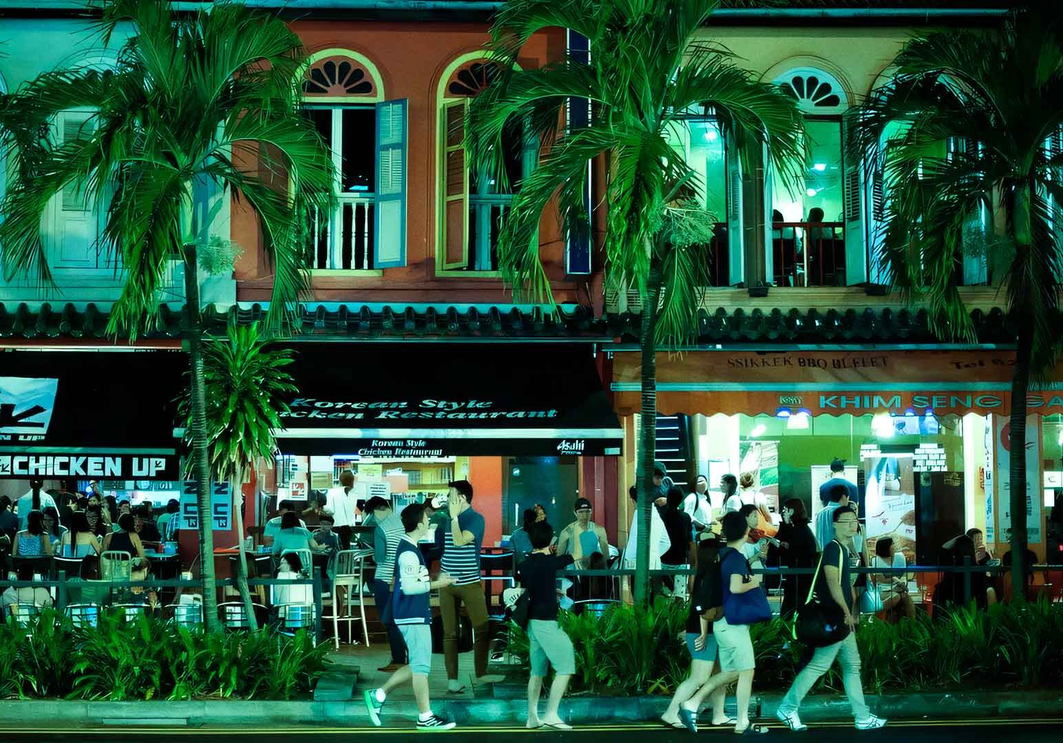 5-Tanjong-Pagar Vibrant Tanjong Pagar nightlife scene with colonial-style shophouses, palm-lined sidewalk restaurants, neon signage for Korean and local eateries, and diners enjoying outdoor seating under green-tinted lights.