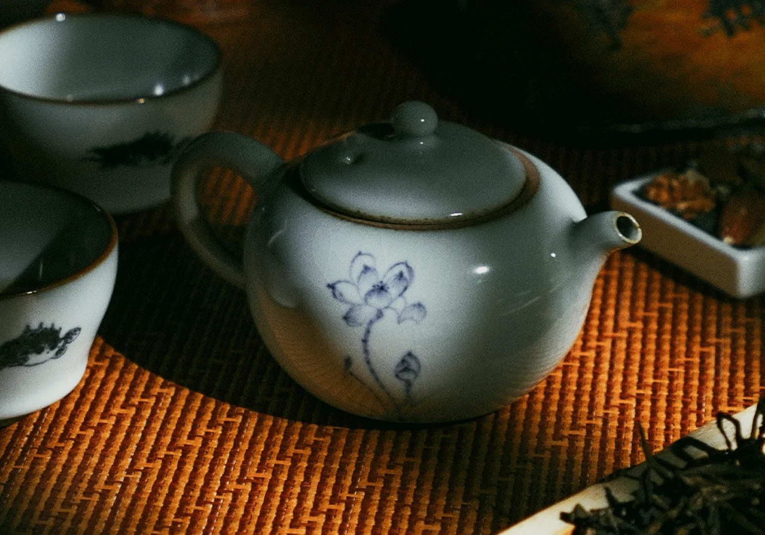 Elegant ceramic teapot and teacups on woven tea mat at Tea Room by Ki-setsu – angled close-up shot highlighting refined teaware and curated luxury tea service