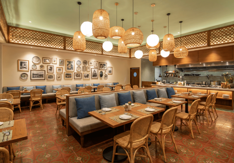 5-restaurant-interior A welcoming dining space featuring patterned terracotta floor tiles, rattan dining chairs, blue accent pillows on banquette seating, and a diverse cluster of woven and globe pendant lights.