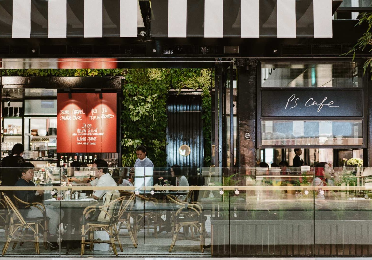 PS.Cafe exterior featuring greenery wall, glass façade, and bistro-style seating.