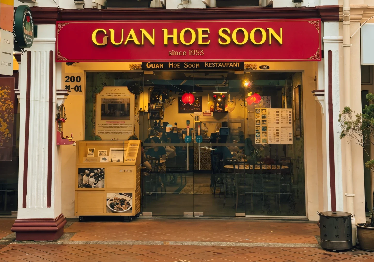 Guan Hoe Soon Restaurant entrance with bold red signage, glass front showcasing tables and décor, and historic Peranakan shophouse design details.