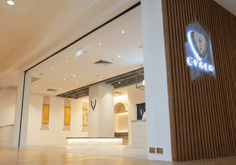The wide, welcoming entrance of Hvala Singapore inside a mall, featuring a prominent illuminated logo on a slatted wood wall and a view into the bright, Japanese-inspired minimalist interior.