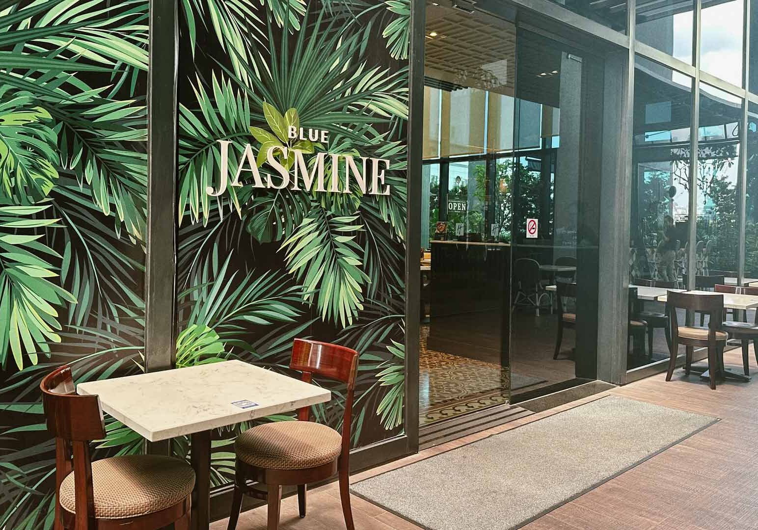 Blue Jasmine restaurant entrance with tropical leaf mural and outdoor table setup.