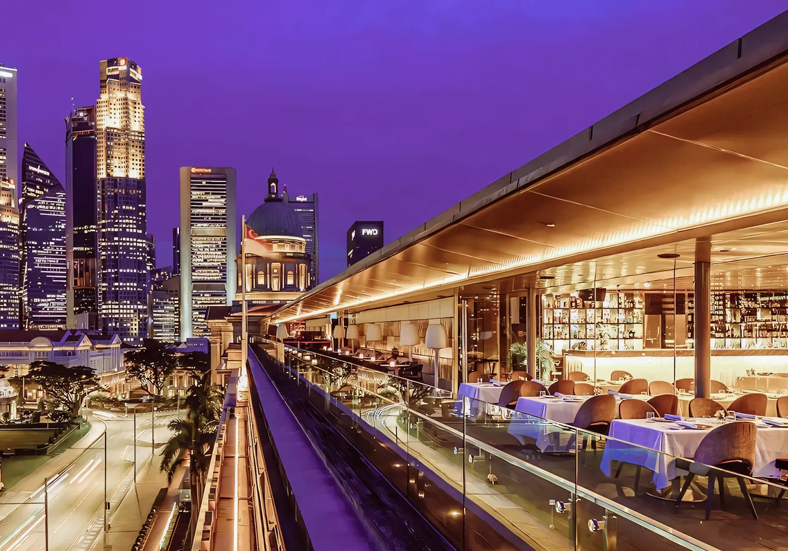 Wide‑angle nighttime shot of a rooftop restaurant at the National Gallery Singapore, featuring an open‑air dining terrace with warm lighting and views of the illuminated Civic District skyline.