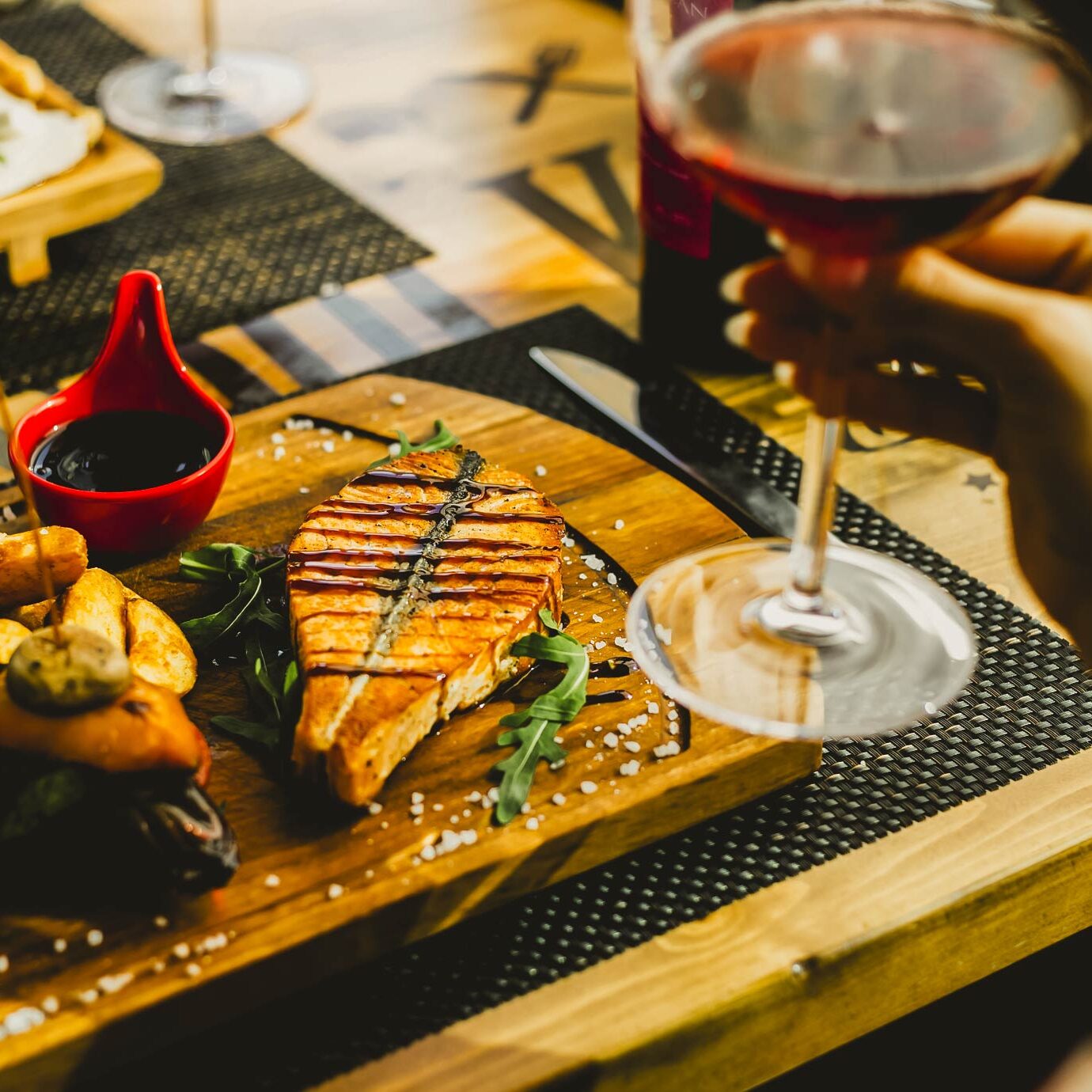 Gourmet grilled salmon steak served with potato wedges and a glass of red wine on a wooden platter.