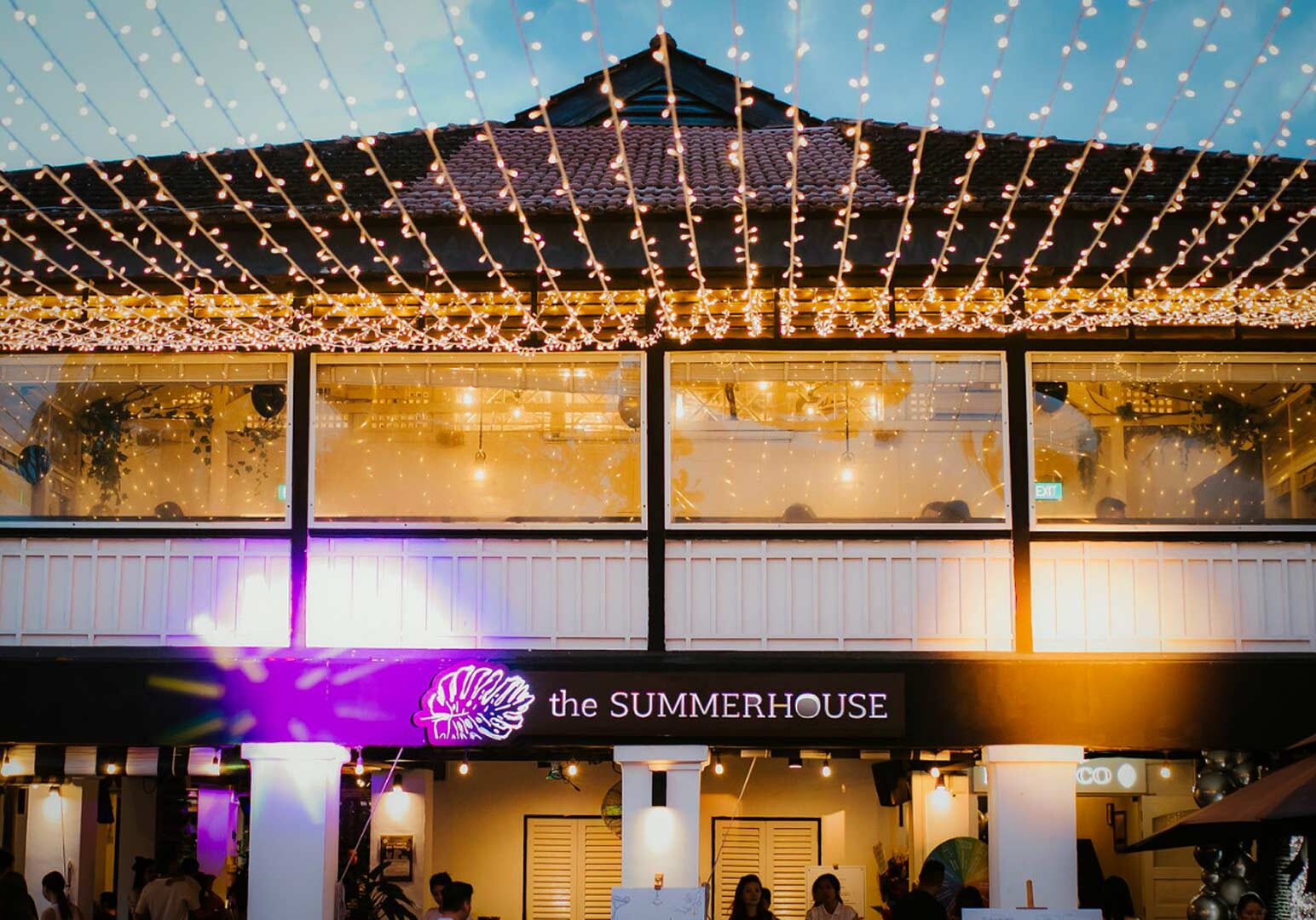 The exterior of The Summerhouse restaurant decorated with strings of warm fairy lights covering the outdoor space, with large windows glowing from indoor lighting.
