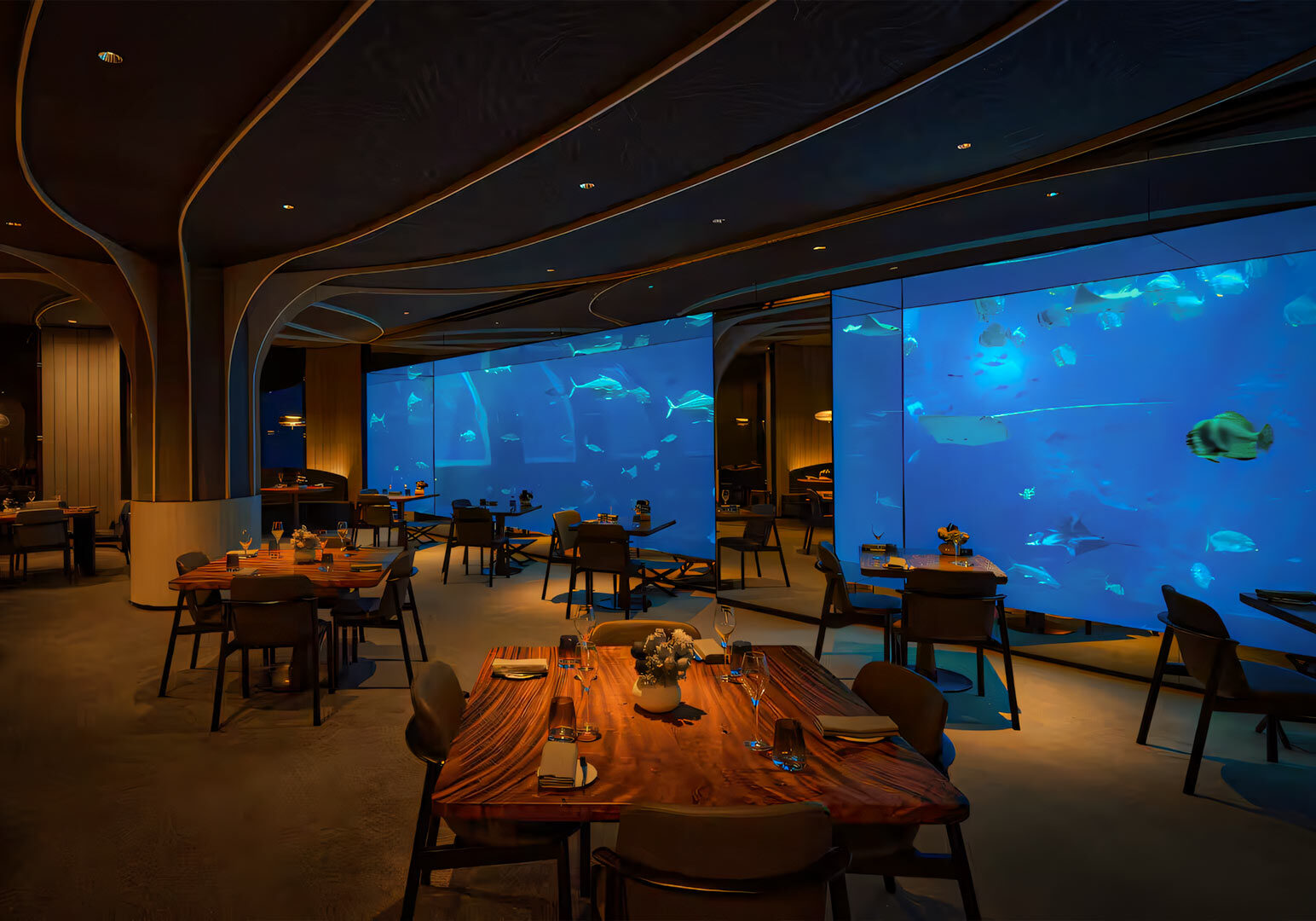 An elegant restaurant interior featuring large aquarium wall panels filled with fish and marine life, with wooden tables set for dining and soft ambient lighting throughout the space.